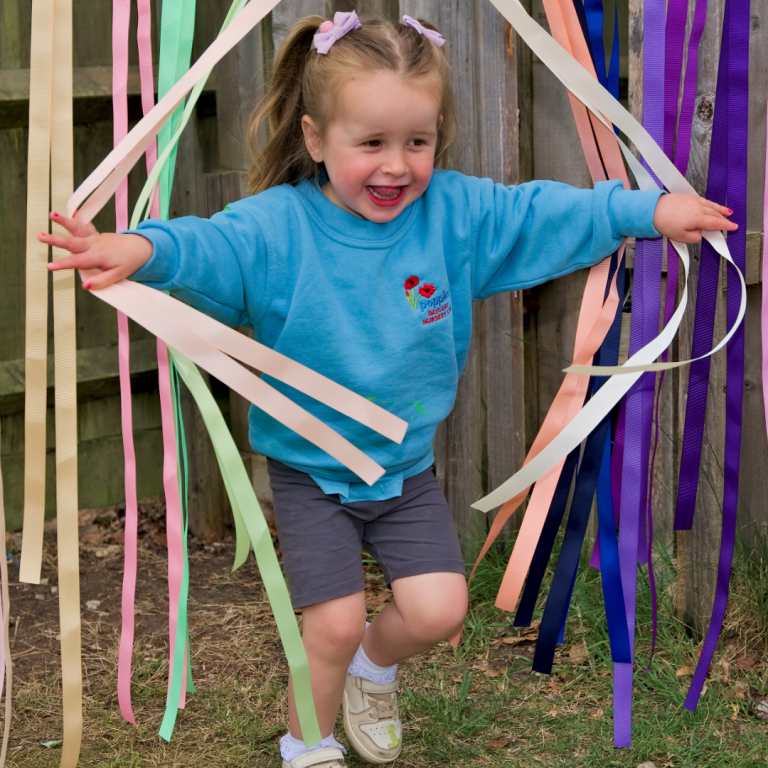 A little girl at Poppies Nursery running through bunting showcasing that when considering How To Choose A Daycare you should see the happiness of the children already there
