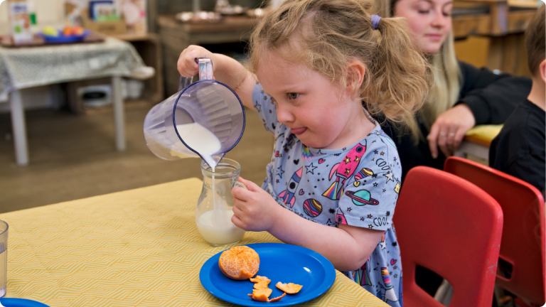 Healthy Eating in the Early Years shown by a 3 year old girl pouring her own milk as a snack