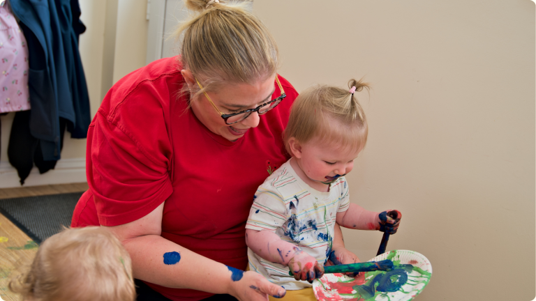 Childminder vs nursery shown here by a Poppies Daycare Nursery practitioner playing with paint as an activity with the 0-2s room