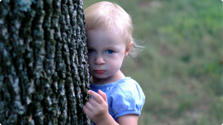 Shy Toddler hiding behind a tree
