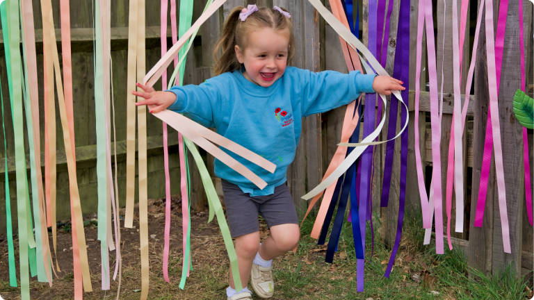 little girl running through streamers showing solitary play as one of the 4 Types of Play in Child Development 