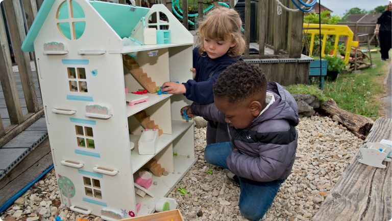 Associative play shown by 2 children playing outsde in a dollshouse showing one of the 4 Types of Play in Child Development