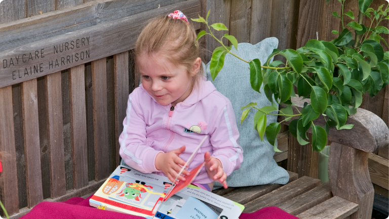 Independent Play for Toddlers shown by a toddler reading on a bench on their own