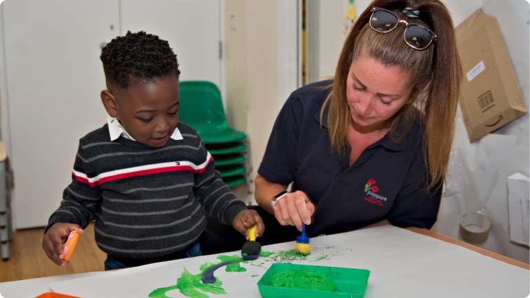 Independent Play for Toddlers shown by a toddler paitning alongside a Poppies Nursery practitioner