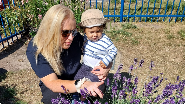 1 Year Old Settling into Nursery: a little boy being held by a nursery worker showing them the lavender