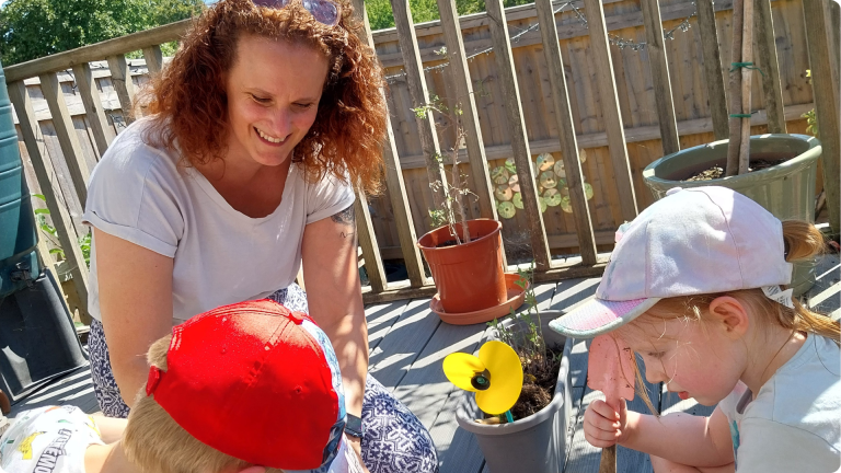 What Do They Teach in Nursery shown by nursery practitioner playing outside teaching the children about growing