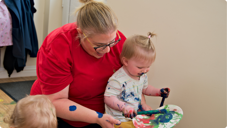 What Do They Teach in Nursery shown by nursery practitioner playing with paint