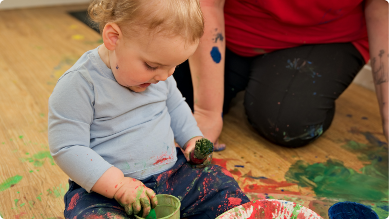 15 Hours Free Childcare shwon by a baby playing with paint
