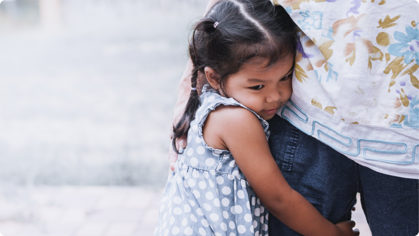 How to Handle Daycare Separation Anxiety shown by a little girl clinging onto her parents leg