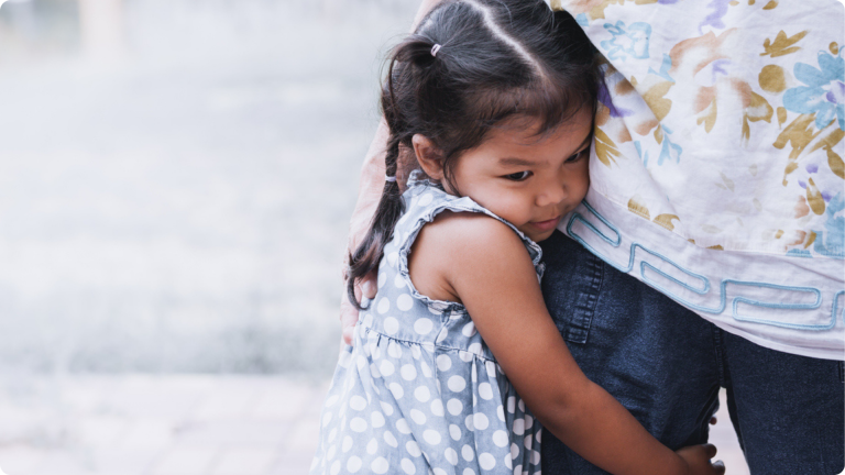 How to Handle Daycare Separation Anxiety shown by a little girl clinging onto her parents leg