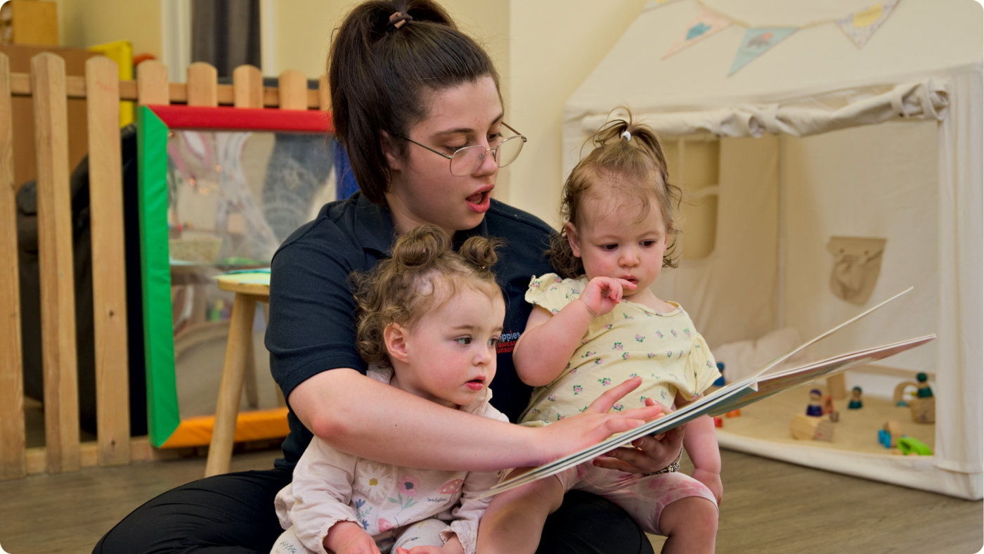Free Childcare Hours Explained - shown by a nursery practitioner reading to two toddlers at Poppies Nursery